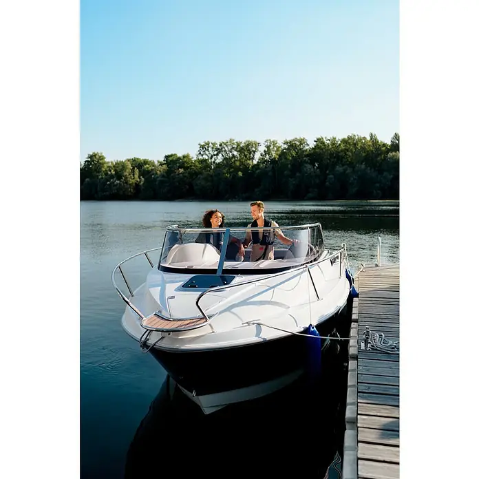PEGAZUS GFK-Boot 550 Comfort - Umfangreiche Zusatzausstattung, Geeignet für: Max. 6 Personen, Nutzlast: 670 kg, CE-Klasse C - Ein elegantes Motorboot liegt an einem Holzsteg, mit zwei Personen an Bord, die das ruhige Wasser und die grüne Umgebung genießen.