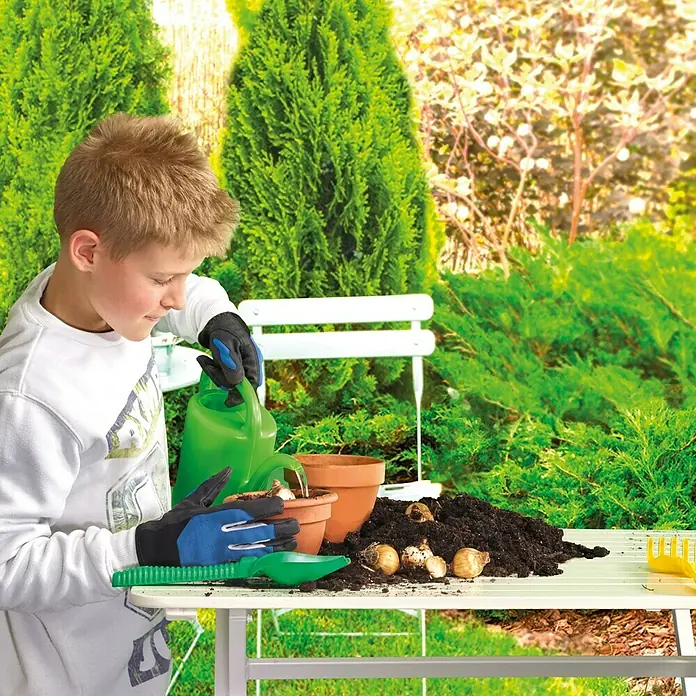 Gardol Kinder-Gartenhandschuhe - 5, Blau - Ein Junge gießt Blumenzwiebeln in einem Topf, umgeben von Gartengeräten und Erde, vor einem grünen Gartenhintergrund.