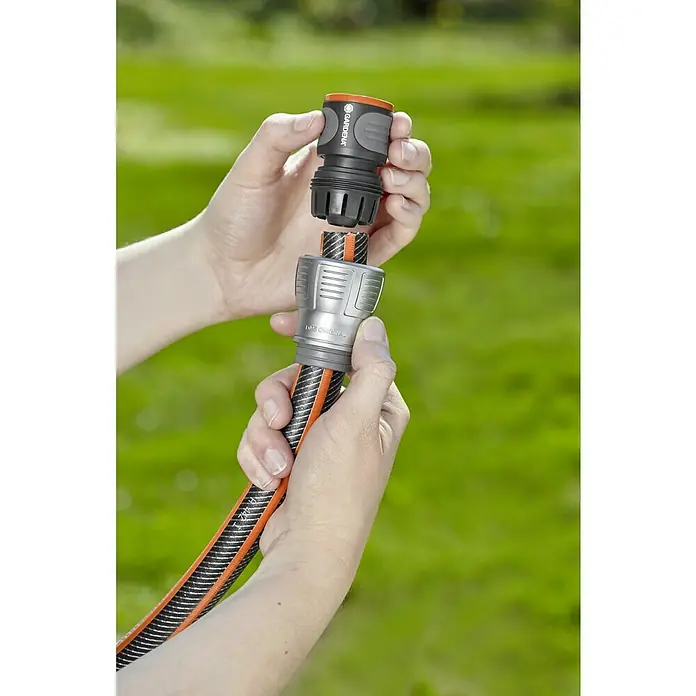 Gardena Schlauchkupplung - Größe: ¾″, Ohne Wasserstopp - Nahaufnahme einer Person, die einen Gardena-Schlauchverbinder an einem Gartenschlauch befestigt, mit grünem Hintergrund.