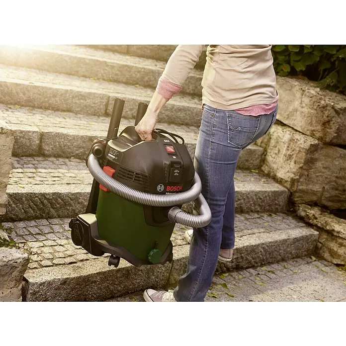 Bosch Elektro-Nass- & Trockensauger AdvancedVac 201.200 W, Behältervolumen: 20 l - Eine Person trägt einen Bosch AdvancedVac 20 Nass- und Trockensauger eine Treppe hinauf, der eine robuste Bauweise und hohe Leistung zeigt.