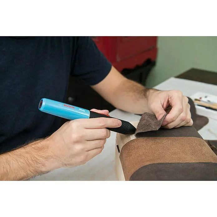 Bosch Akku-Heißklebestift Gluey - Farbe: Lagoon Blue - Nahaufnahme von Handwerkern, die mit einem Bosch Gluey Klebestift Leder auf ein Holzprojekt kleben, wobei der Fokus auf Präzision liegt.