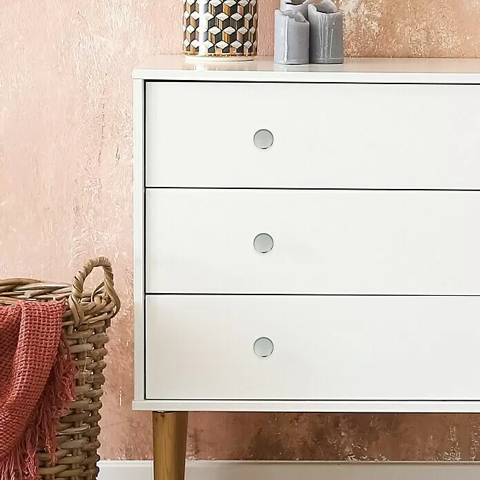 Häfele Pomo para muebles - Tipo de tirador del mueble: Botón, Ø x Al: 34 x 27 mm, Cromado - Cómoda blanca con tres cajones y pomos plateados, junto a una cesta de mimbre con una manta roja, en un ambiente acogedor.