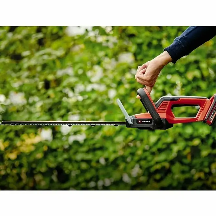 Einhell Power X-Change 18V Akku-Heckenschere GC-CH 18/40 Li Solo - 18 V, Li-Ionen, Ohne Akku, Schnittlänge: 40 cm - Abbildung einer roten Einhell-Akku-Heckenschere in Aktion, gehalten von einer Hand vor grünem Hintergrund.