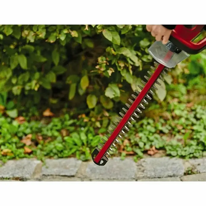Einhell Power X-Change 18V Akku-Heckenschere GC-CH 18/40 Li Solo - 18 V, Li-Ionen, Ohne Akku, Schnittlänge: 40 cm - Eine rote Heckenschere wird von einer Hand gehalten, im Hintergrund grünes Blattwerk. Fokus liegt auf der Schärfe der Klingen der Heckenschere.