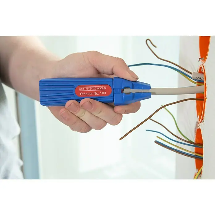 Weicon Stripper No. 100 - Verwendung: Abmanteln - Eine Hand, die einen blauen Weicon Tools Stripper No. 100 zum Abisolieren eines Kabels an einer Wand mit elektrischen Leitungen verwendet.