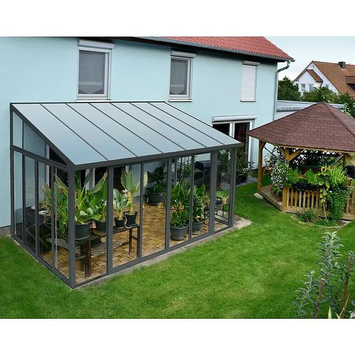Palram – Canopia Wintergarten San Remo - B x T x H: 4,25 x 3 x 3,1 m, Anthrazitgrau - Ein Gewächshaus aus Glas mit einem schwarzen Rahmen, gefüllt mit grünen Pflanzen, steht neben einem Holzpavillon in einem Garten.