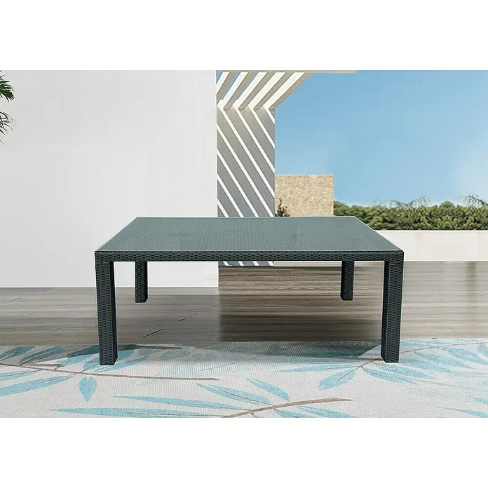 Sunfun Mesa de jardín Neila - L x An x Al: 180 x 100 x 75 cm, Aluminio/Ratán sintético, Gris plata - Una mesa de patio gris con tapa de vidrio se sitúa sobre una alfombra estampada en el exterior con un edificio al fondo.