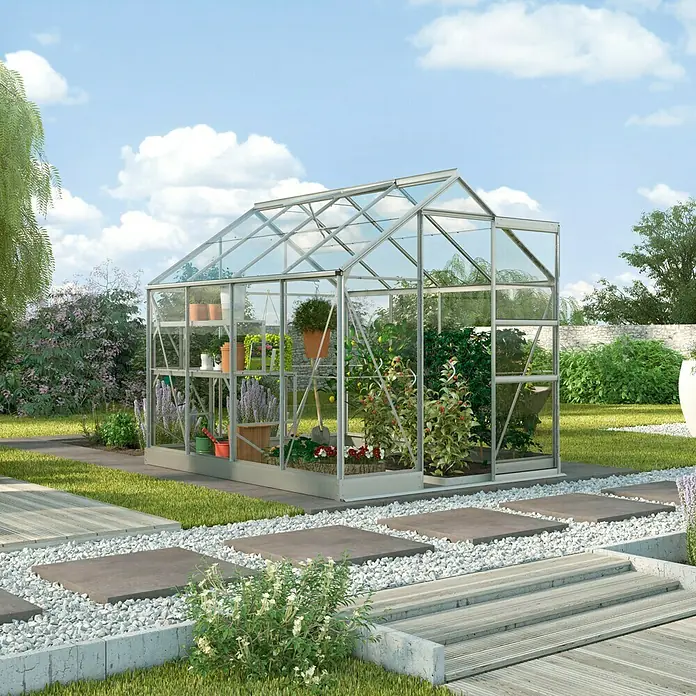 Vitavia Gewächshaus Eris 6200Außenmaß inkl. Dachüberstand (B x T): 195 x 323 cm, 3 mm, Silbergrau - Ein Gewächshaus mit Pflanzen und Regalen im Inneren, umgeben von einem Garten mit Gras und Steinen.