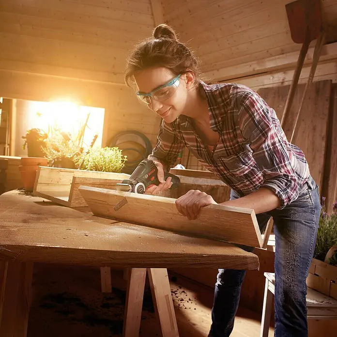 Bosch Power for All 12V NanoBlade-Säge EasyCut 12 - 12 V, Ohne Akku, Leerlaufdrehzahl: 4.100 U/min - Frau arbeitet mit einem Bosch Multifunktionswerkzeug an einem Holzstück. Das Werkzeug ist kompakt und vielseitig.