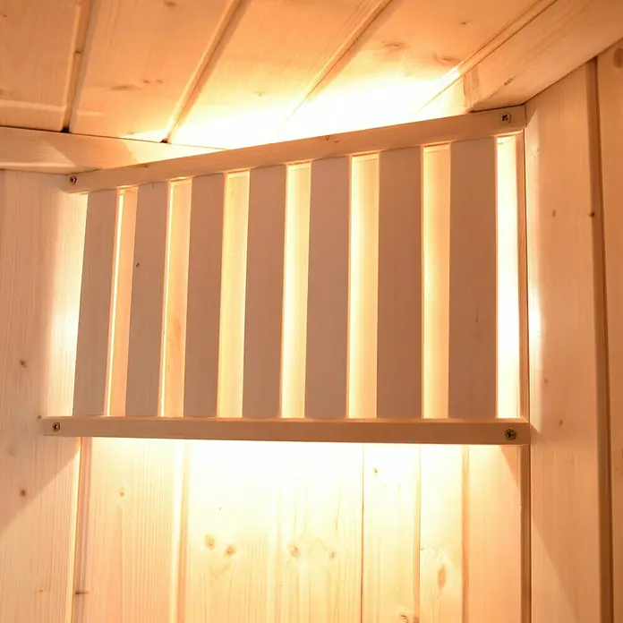 Weka Massivholzsauna Cubilis 3 GTF - Ohne Ofen, L x B x H: 195 x 245 x 205 cm - Nahaufnahme einer hölzernen Saunaleuchte. Das Licht scheint durch die Holzlamellen und erzeugt eine warme Atmosphäre.