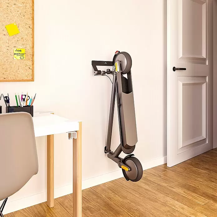 Rei Wandträger - Geeignet für: E-Scooter, L x B x H: 100 x 320 x 130 mm - Ein zusammengeklappter dunkelgrauer Elektroroller mit gelben Akzenten, an einer Wand neben einem Holzschreibtisch montiert, zeigt kompakte Lagerung.