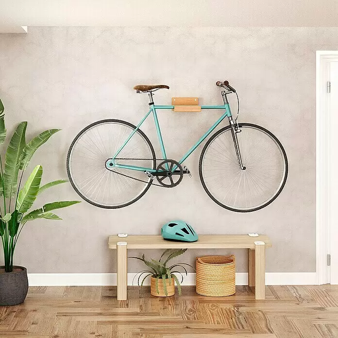 Rei Fahrradhalterung - L x B x H: 35 x 20 x 10 cm, Belastbarkeit: 25 kg - Türkisblaues Fahrrad an heller Holz-Wandhalterung, über einer Holzbank mit türkisblauem Helm und Pflanzen.