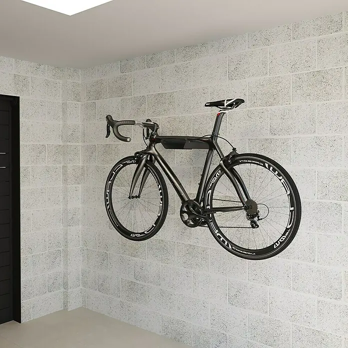 Rei Fahrradhalterung - L x B x H: 365 x 280 x 85 mm - Ein Rennrad hängt an einer Wandhalterung in einem Raum mit weiß gestrichenen Ziegelwänden.