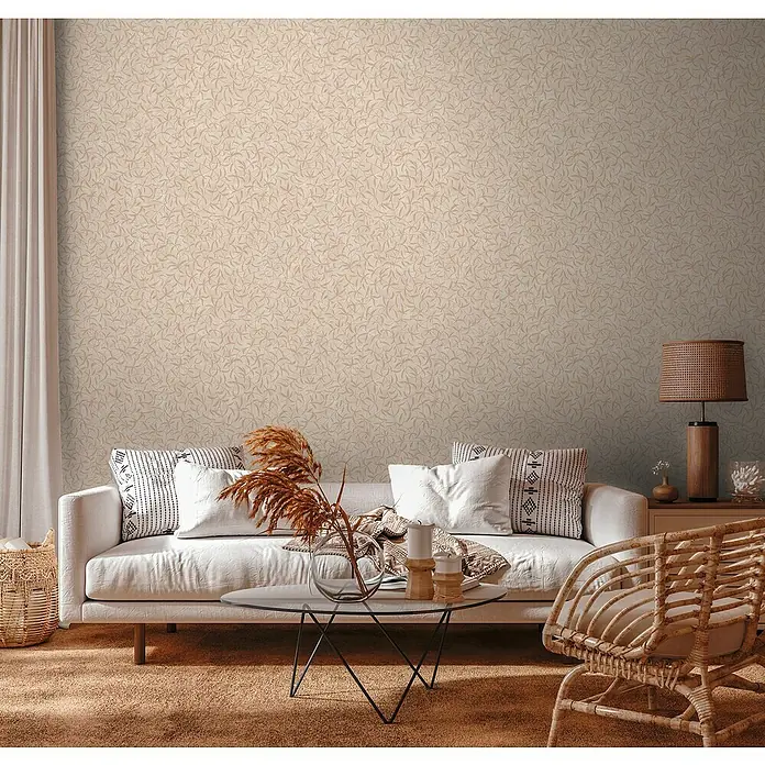 A.S. Création Vliestapete Blättchen - Alloverbeige, Floral, 10,05 x 0,53 m - Einladendes Wohnzimmer mit beigem Musterhintergrund, Sofa, Kissen und einem Rattansessel.