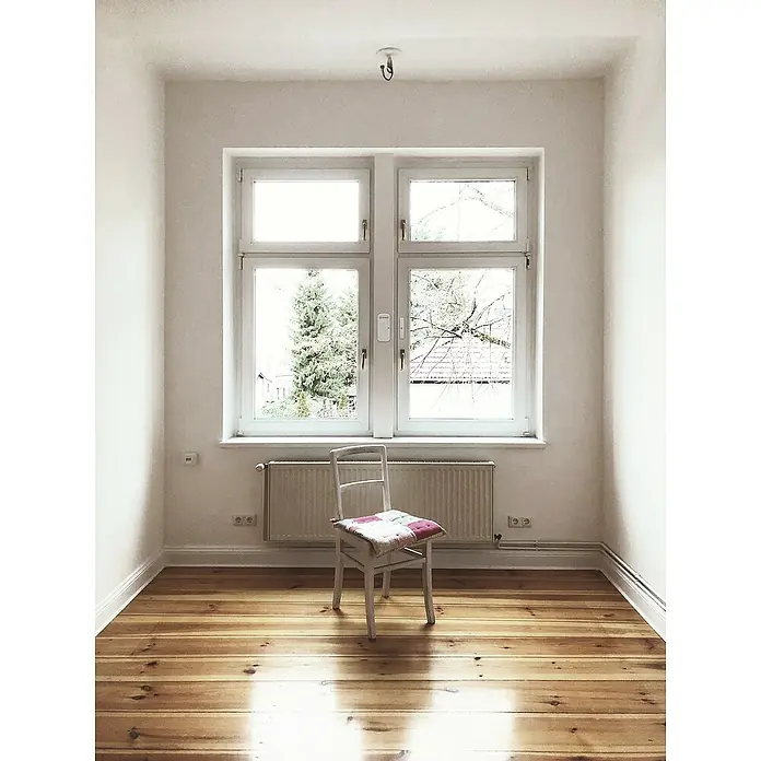 Ledvance Smart+ WiFi Funk-Fensterkontakt - Weiß, 3,1 x 2,4 x 7,2 cm - Heller Raum mit einem weißen Stuhl mit gestepptem Sitzkissen vor einem Fenster und einem Heizkörper. Der Boden ist aus hellem Holz.