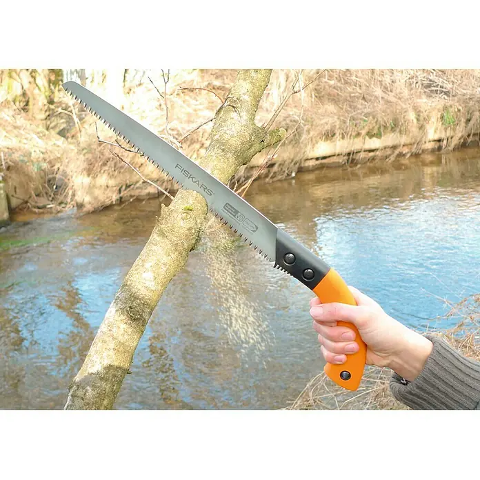 Fiskars Hand-Astsäge SW84 - Länge: 54,3 cm, Max. Aststärke: 12 mm, Orange/Schwarz - Astsäge Fiskars mit orangem Griff schneidet einen Baum am Flussufer.