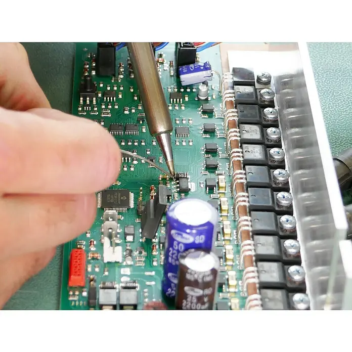 Weller Lötstation WE1010 digital - ESD sicher - Höchsttemperatur: 450 °C - Detailaufnahme einer Hand, die mit einem Lötkolben an einer grünen Elektronikplatine arbeitet, zur Reparatur elektronischer Geräte.