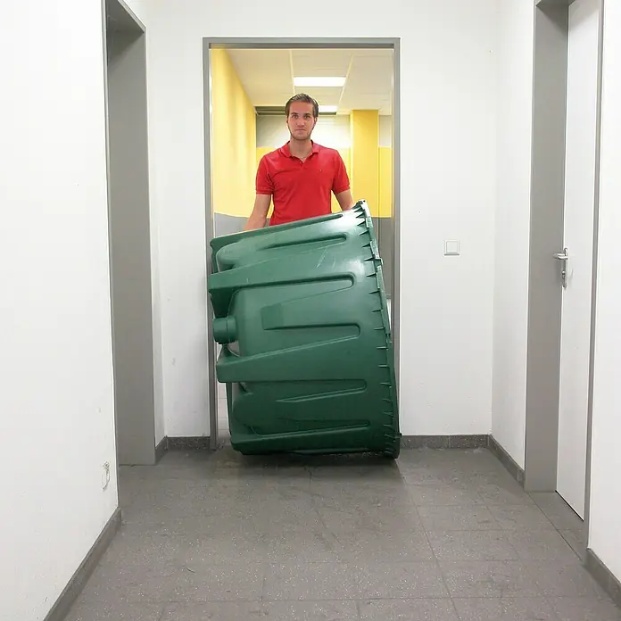 4rain Zisterne Herkules - Gesamt Fassungsvermögen: 4.800 l, 3 Stk., Dunkelgrün - Mann transportiert einen großen grünen Behälter durch einen Flur. Der Behälter dominiert das Bild und füllt fast den gesamten Durchgang.
