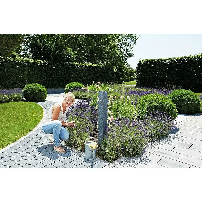 Garantia Wasserzapfstelle Granit - Darkgranite, Höhe: 100 cm - Frau gärtnert im üppigen Garten mit Lavendel und akkurat geschnittenen Büschen, während eine stilvolle Bewässerung bereitsteht.