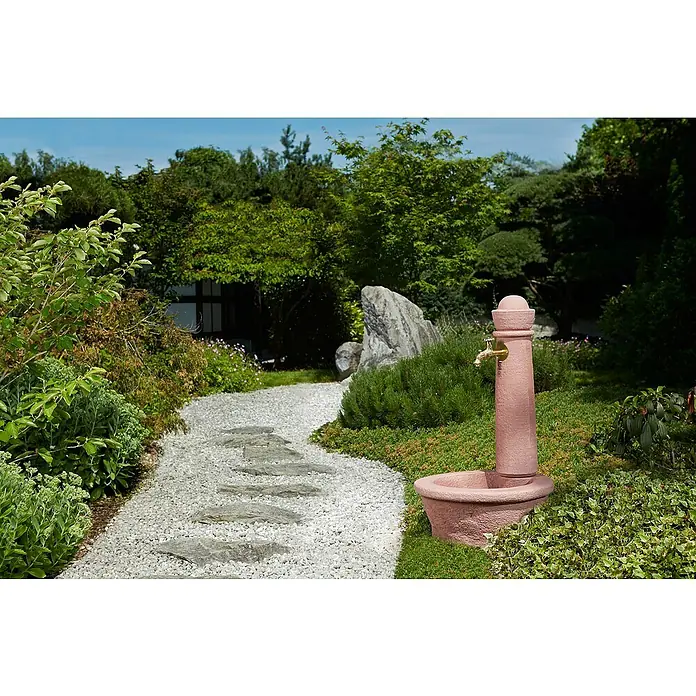 Garantia Brunnen Roma - Redstone, 54 x 54 x 100 cm - Eine verzierte Sandstein-Gartenwasserstelle mit goldenem Hahn steht in einem üppigen, friedlichen Garten mit einem Kiesweg und grünen Pflanzen.