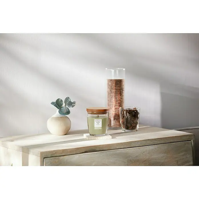 Woodwick Nature's Wick Duftkerze - Im Glas, White Pepper, Anzahl Dochte: 1 Stk. - Nahaufnahme einer Nature's Wick Duftkerze mit Holzdeckel auf einer Kommode, neben einer Vase und dekorativen Gläsern.