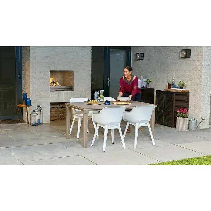 Allibert Gartensessel Akola im Set - Polypropylen, Weiß, B x T x H: 56,5 x 50 x 80 cm - Terrasse mit Esstischgruppe. Eine Frau deckt den Tisch. Im Hintergrund ein Kamin und Dekoration.
