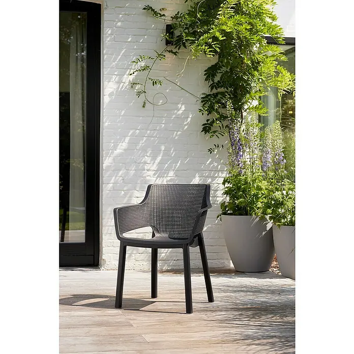 Keter Silla de jardín Elisa - 53 x 62 x 78,4 cm, Polipropileno, Antracita - Elegante imagen de una moderna silla de jardín negra en un patio de madera, con una pared de ladrillo blanco y vegetación exuberante.