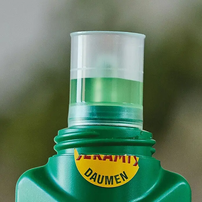 Seramis Flüssigdünger - 500 ml, Geeignet für: Blühpflanzen - Nahaufnahme einer grünen Flasche Jeramix Daumen mit Messbecheraufsatz, teilweise gefüllt mit grüner Flüssigkeit, vor verschwommenem Hintergrund.