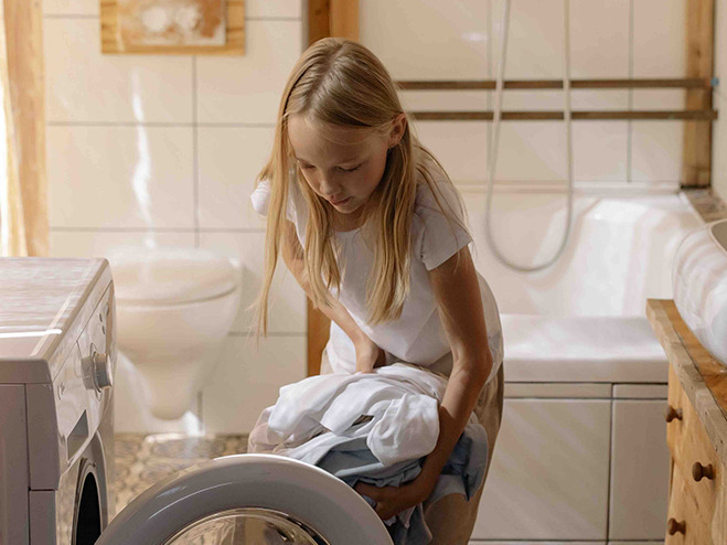 Mädchen befüllt Waschmaschine im Badezimmer