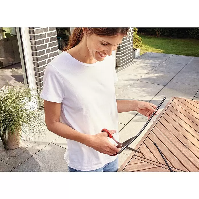 Tesa Insect Stop Lamellenvorhang Premium - B x H: 95 x 220 cm - Frau schneidet schwarzes biegsames Band mit rot-griffiger Schere.