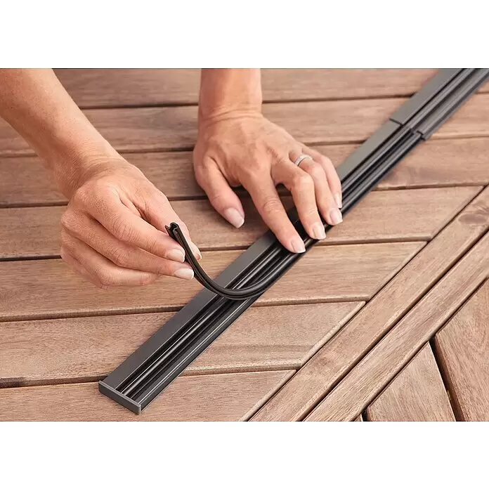 Tesa Insect Stop Lamellenvorhang Premium - B x H: 95 x 220 cm - Hände montieren eine dunkle, flexible Kabelabdeckung in eine Mehrkanal-Schiene auf Holz.