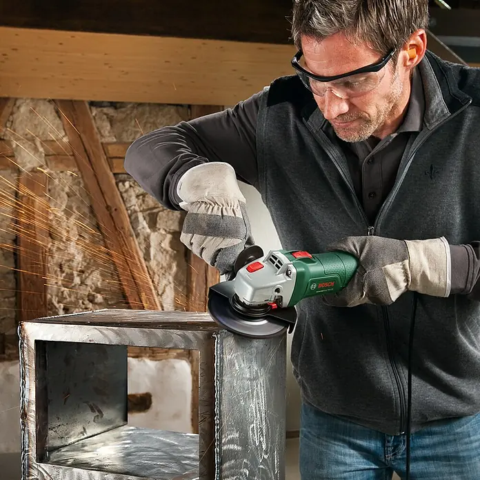 Bosch Elektro-Winkelschleifer UniversalGrind 750-125 - 750 W, Durchmesser Scheibe: 125 mm, Leerlaufdrehzahl: 12.000 U/min - Ein Mann benutzt einen Bosch Winkelschleifer, um Metall zu bearbeiten. Funken fliegen, während er die Oberfläche glättet.