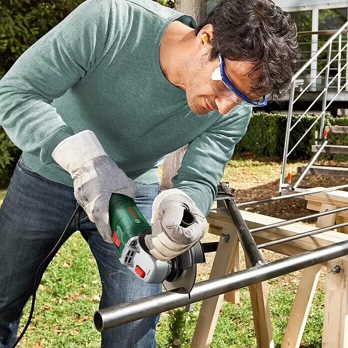 Bosch Elektro-Winkelschleifer UniversalGrind 750-125 - 750 W, Durchmesser Scheibe: 125 mm, Leerlaufdrehzahl: 12.000 U/min - Mann schneidet Metallrohr mit grün-grauem Bosch Winkelschleifer im Freien.