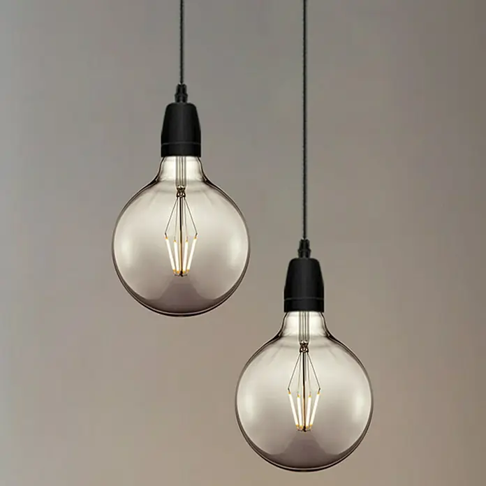 Home Sweet Home LED-Lampe Vintage Globe-Form E27 - E27, Dimmbar, Warmweiß, 120 lm, 4 W - Zwei dekorative Pendelleuchten mit rauchfarbenen Glühbirnen und schwarzen Fassungen hängen von der Decke.