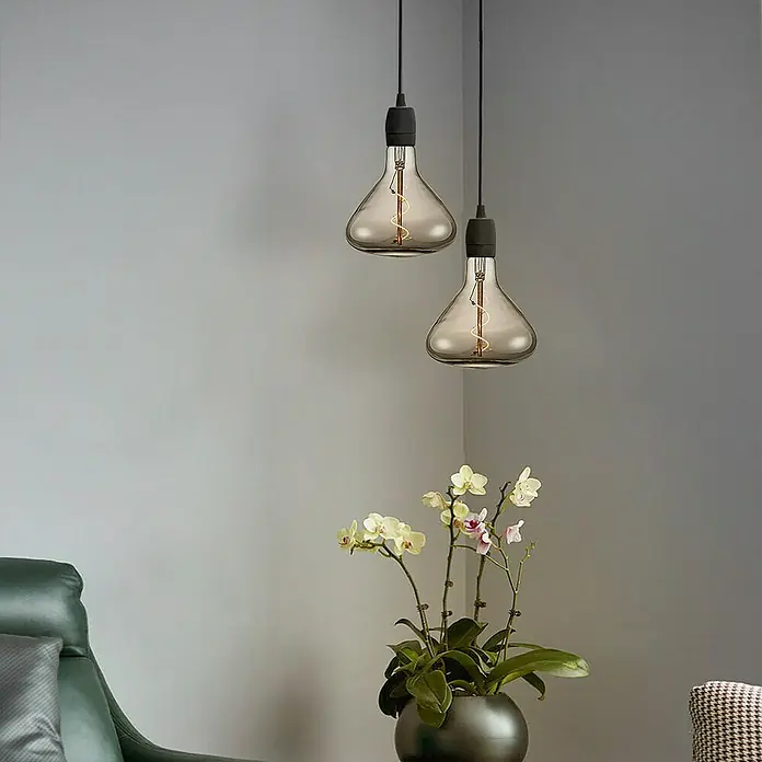 Home Sweet Home LED-Lampe Vintage Globe-Form E27 - E27, Dimmbar, Warmweiß, 20 lm, 3 W, Farbe: Smoky - Elegante graue Glühbirnen mit sichtbarem Glühfaden hängen über einer Orchidee, die eine warme Atmosphäre in dem modern eingerichteten Raum schaffen.