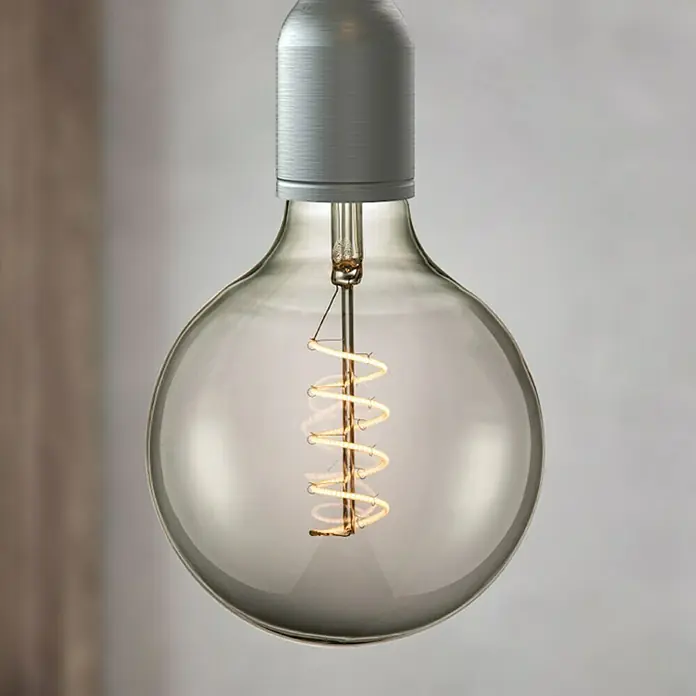 Home Sweet Home LED-Lampe Vintage Globe-Form E27 - E27, Dimmbar, Warmweiß, 140 lm, 4 W - Nahaufnahme einer dekorativen Glühbirne mit einem spiralförmigen Glühfaden und einem silbergrauen Sockel, die ein warmes, einladendes Licht ausstrahlt.