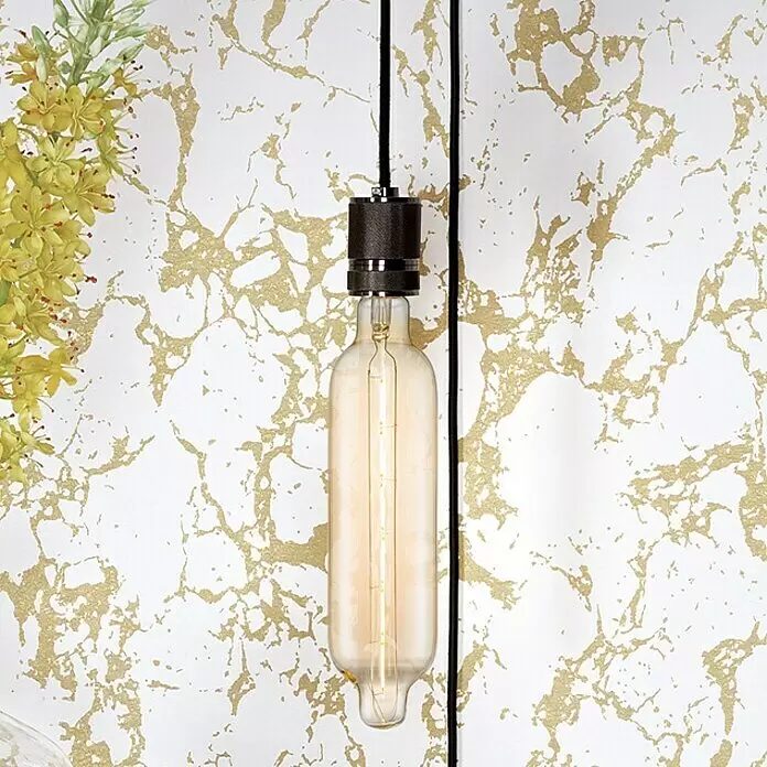 Home Sweet Home LED-Lampe Edison - E27, Dimmbar, Warmweiß, 250 lm, 5 W, Kapsel - Lange Edison-Stil LED-Glühbirne mit dunkler Metallfassung, hängend vor einer gold-weiß gemusterten Wand mit Grünpflanzen.