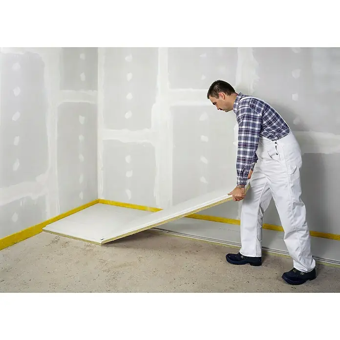Fermacell Estrichelement - 1.500 x 500 x 30 mm, Mineralwolle/Gipsfaser - Ein Mann in Arbeitskleidung verlegt eine isolierte Bodenplatte. Das Fertigteil besteht aus einer Gipsfaserplatte und einer Dämmschicht.