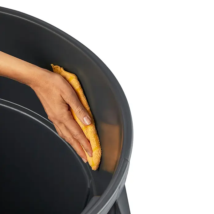 Rotho Standard-Mülleimer Titan - 85 l, Kunststoff, Grau - Detailaufnahme eines Abfallbehälters, der mit einem gelben Tuch gereinigt wird, Fokus auf Sauberkeit und Pflege des Produkts.