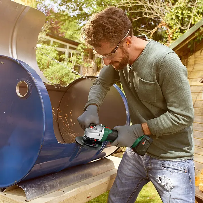 Bosch Power for All 18V Akku-Winkelschleifer AdvancedGrind 18V-80 - 18 V, Ohne Akku, 125 mm, 2.800 U/min - 12.000 U/min - Ein Mann benutzt einen Bosch-Winkelschleifer, um Metall zu schneiden. Die Funken sprühen, während er präzise arbeitet, mit Schutzbrille und Handschuhen.