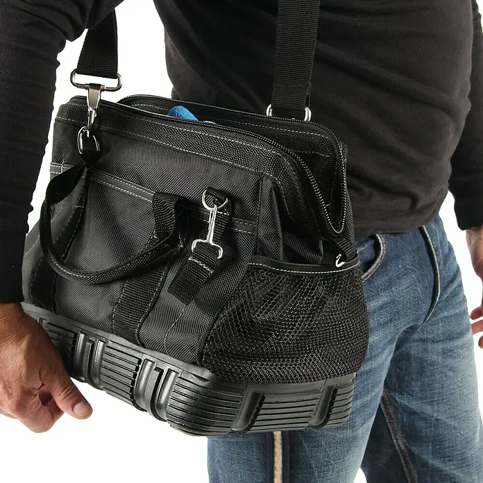 Hepco & Becker Werkzeugtasche Polytex 5854 - L x B x H: 195 x 340 x 260 mm, Polyester - Ein Mann trägt eine schwarze Werkzeugtasche mit Schultergurt, die auf einem robusten, geformten Sockel steht, ideal für den Transport von Werkzeugen.