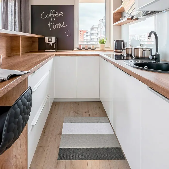 Alfombra de vinilo Living Stripes - Gris, 90 x 60 cm - Una cocina moderna con armarios blancos, encimera de madera y una alfombra de rayas que añade un toque de color al espacio.