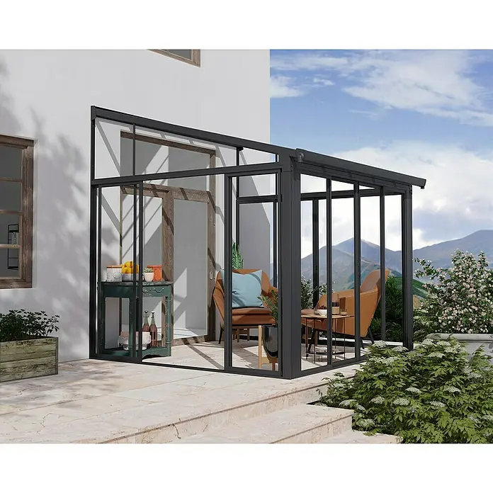 Palram – Canopia Wintergarten San Remo - B x T x H: 3,05 x 3 x 3,1 m, Anthrazitgrau - Bild einer modernen Terrassenüberdachung mit dunklem Rahmen, die einen gemütlichen Außenbereich mit Möbeln und Grünpflanzen bietet.