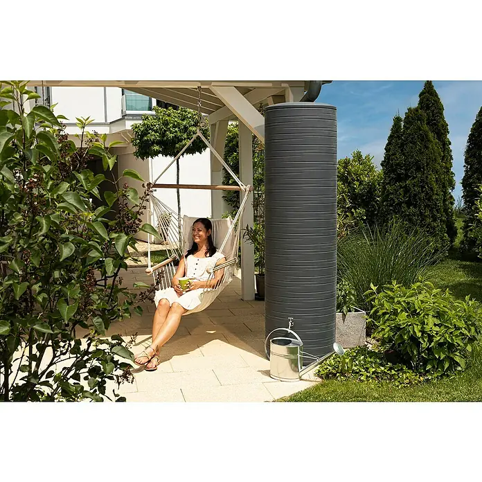 Arves Regenspeicher Novara - 500 l, Anthrazit - Draußen entspannen: Eine Frau genießt einen Drink in einer Hängematte neben einem eleganten grauen Regenspeicher, der perfekt in den Garten passt.