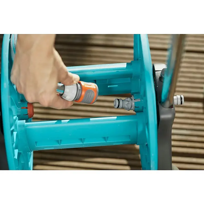 Gardena Carro portamangueras Cleveroll S - Plástico/metal, Capacidad de manguera: 40 m, 13 mm (½″) - Primer plano de un carro portamangueras turquesa claro con una pieza de manguera naranja-gris que se une a un conector gris.