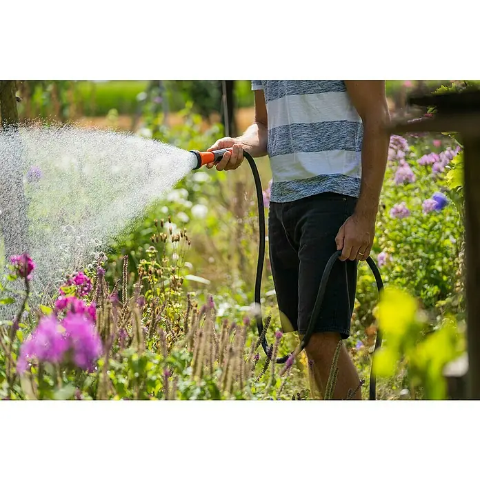 Gardena Gartenschlauch Liano Life - 10 m, Schlauchdurchmesser: 13 mm - Ein Mann bewässert mit einem Gartenschlauch seinen Garten, wobei der Schlauch und der Wasserstrahl im Fokus stehen.