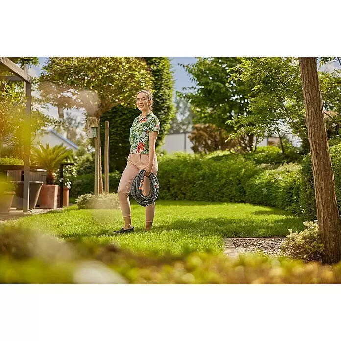 Gardena Gartenschlauch Liano Life Set - 30 m, Schlauchdurchmesser: 13 mm - Frau hält aufgerollten grauen Gartenschlauch mit orangefarbenen Anschlüssen in grünem Garten.