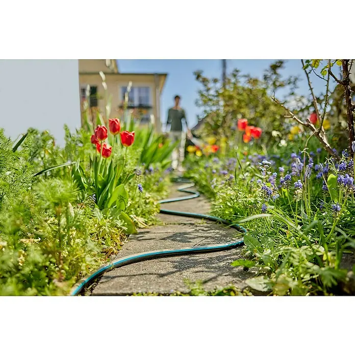 Gardena EcoLine Gartenschlauch - 20 m - Eine blaue Gartenschlauch liegt auf einem gepflasterten Weg, umgeben von üppigen Blumen und Grünpflanzen. Bewässerung leicht gemacht.