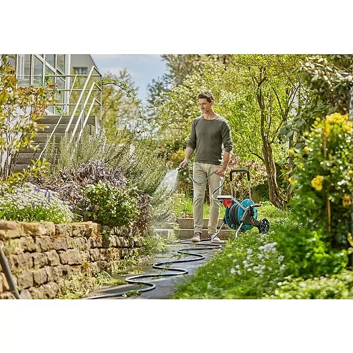 Gardena EcoLine Gartenschlauch - 20 m - Ein Mann bewässert Pflanzen in einem Garten mit einer blau-schwarzen Gardena Schlauchtrommel mit Rädern.
