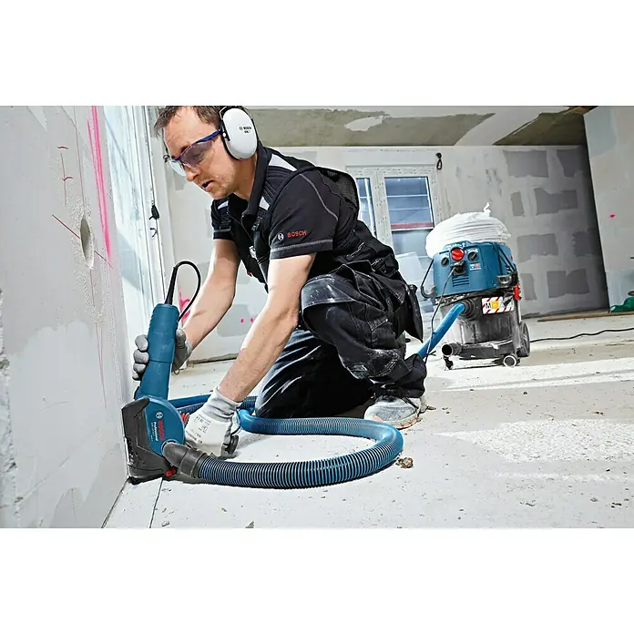 Bosch Professional Absaugvorrichtung GDE 125 EA-T - Passend für: Bosch Winkelschleifer GWS-Serie mit Ø 125 mm - Ein Handwerker, der mit einem Bosch Mauernutfräse an einer Wand arbeitet, während ein Staubsauger den Staub absaugt.